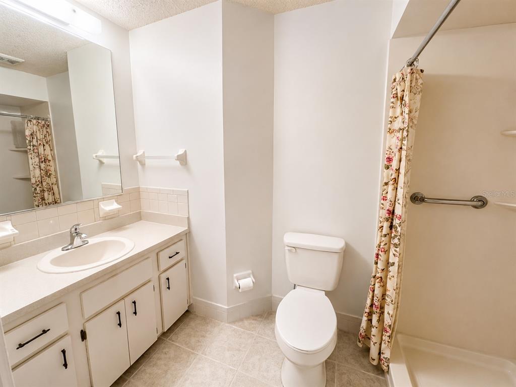 A bathroom features a white vanity, a toilet, and a shower with a floral curtain — 8565 SW 109TH STREET, OCALA, FL
