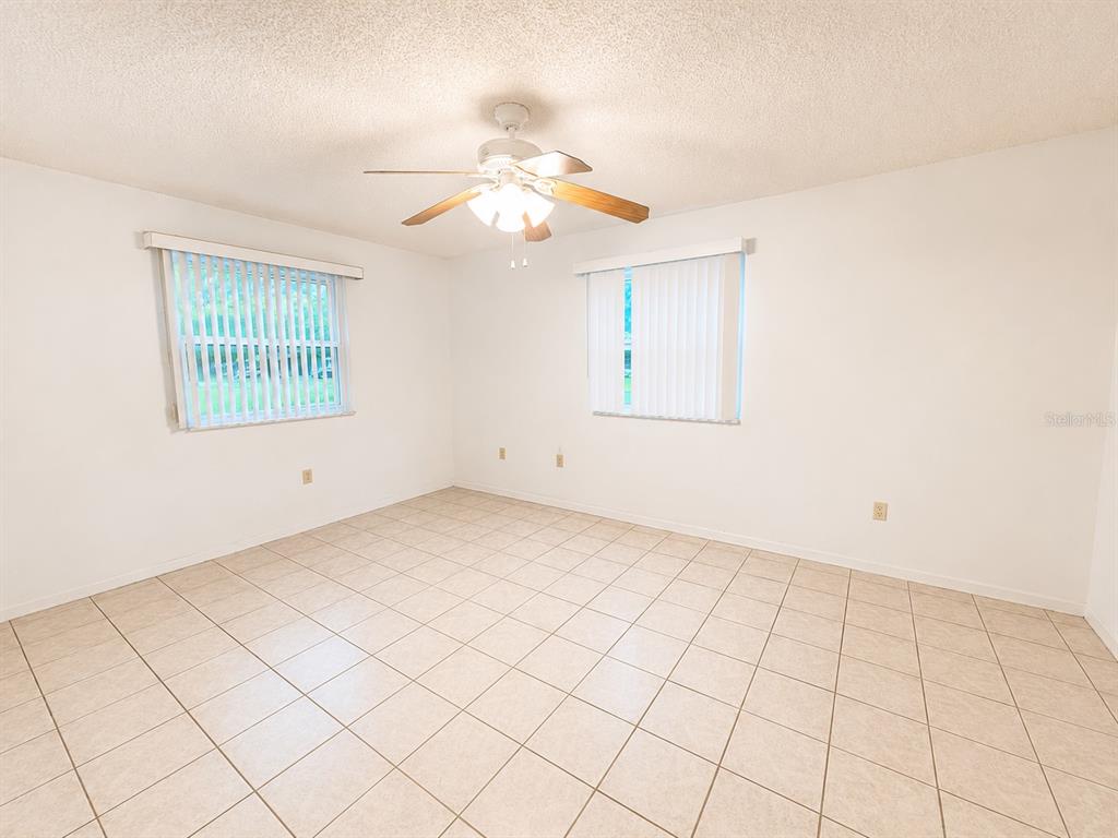 An empty bedroom features white walls, tile flooring, a ceiling fan, and two windows — 8565 SW 109TH STREET, OCALA, FL
