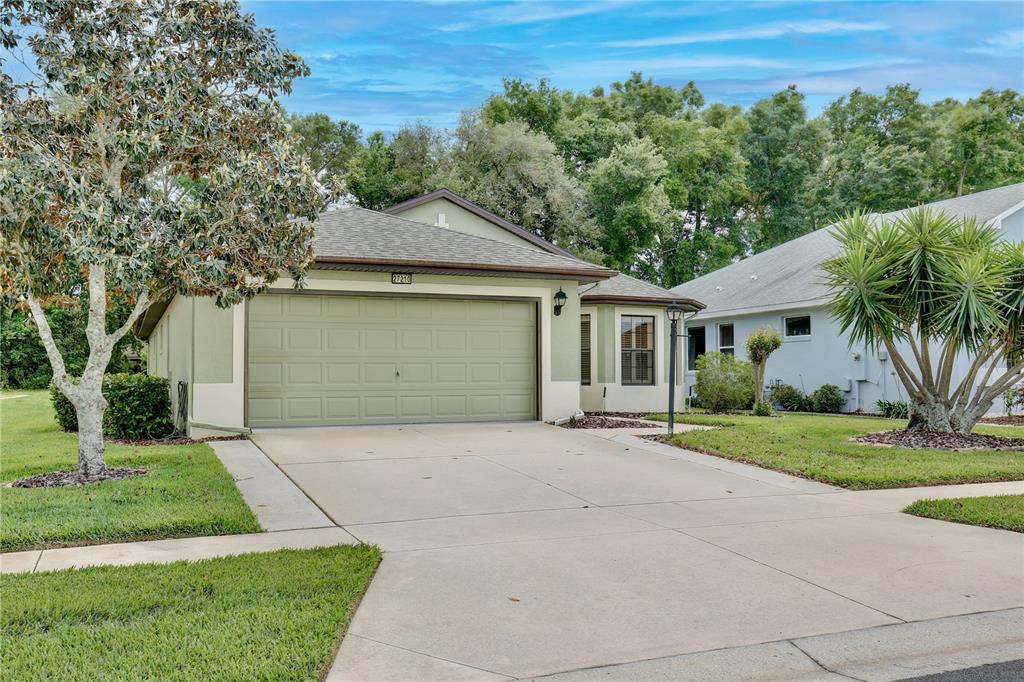 A single-story house with a green garage door, light-colored stucco walls, and a concrete driveway — 27210 STONEY BROOK DRIVE, LEESBURG, FL