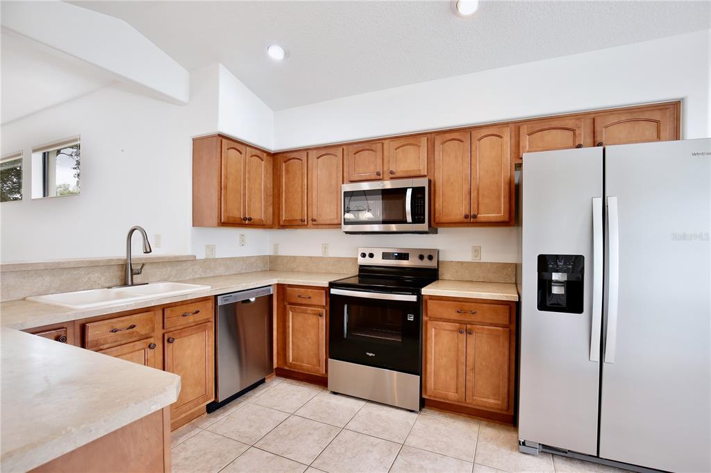 A kitchen with wood cabinets, stainless steel appliances, and light-colored countertops and tile flooring — 27210 STONEY BROOK DRIVE, LEESBURG, FL