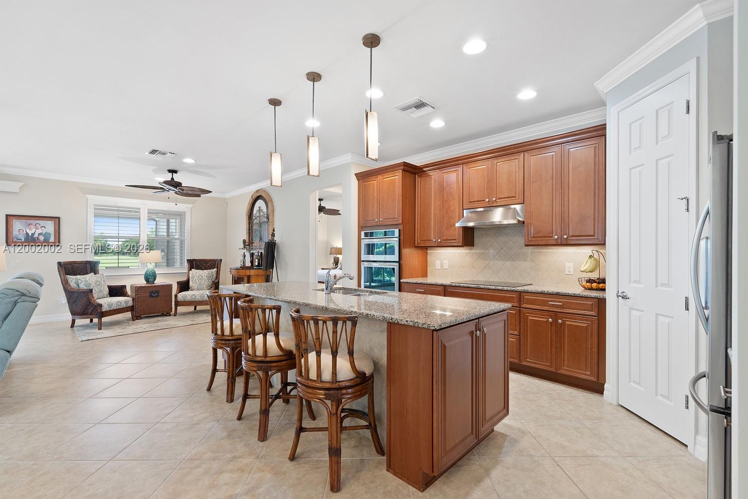 A kitchen features wood cabinets, granite countertops, a central island with bar stools, and tile floors — 6392 Liberty St, Ave Maria FL 34142, AVE MARIA, FL