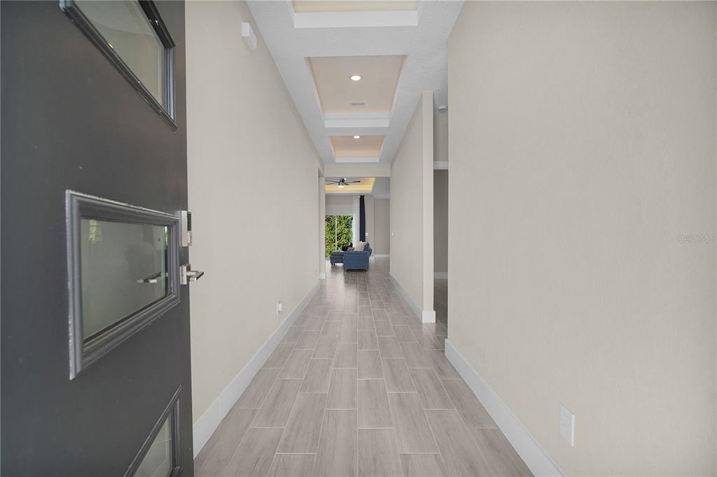 A long hallway with tray ceilings and light wood-look tile flooring leads to a living area — 1187 N PLATTE LANE, POINCIANA, FL