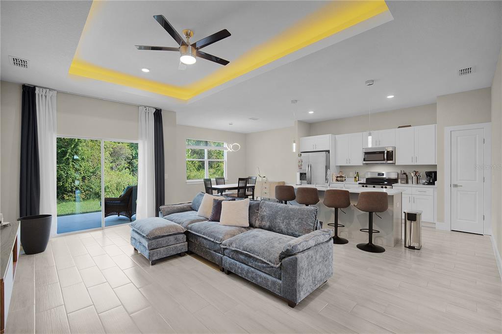 An open-concept living room and kitchen feature light tile floors, a tray ceiling, and furniture — 1187 N PLATTE LANE, POINCIANA, FL