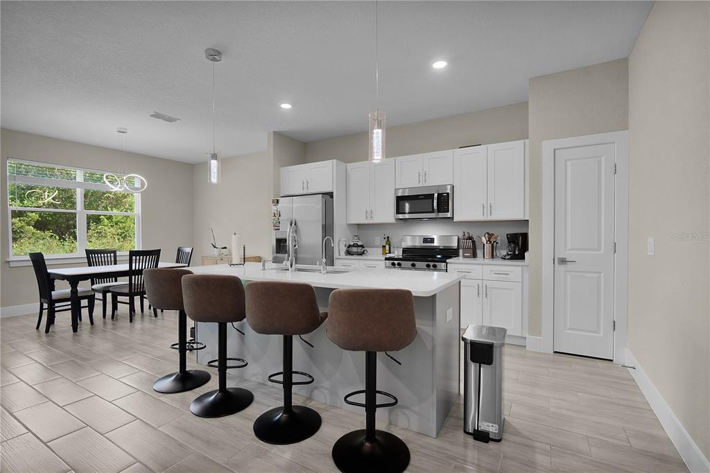 A modern kitchen features white cabinetry, a large island with bar stools, and tile flooring — 1187 N PLATTE LANE, POINCIANA, FL