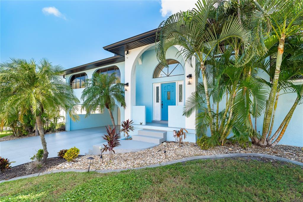 A light blue two-story house features a covered entryway, arched windows, and surrounding palm trees — 10467 MARION STREET, ENGLEWOOD, FL