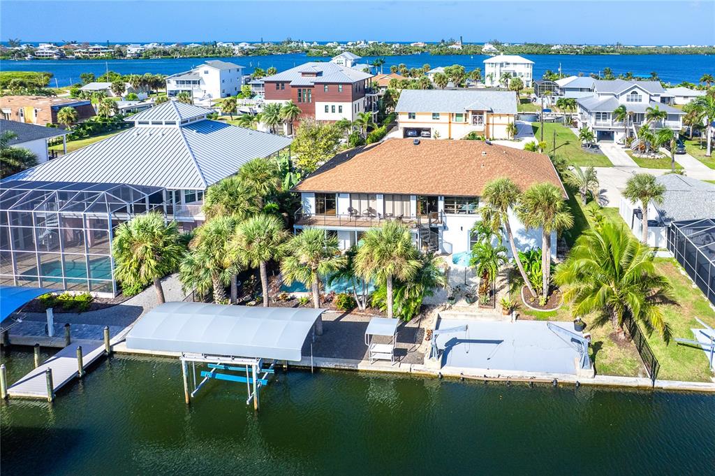 An aerial view shows a waterfront house with a pool, boat lift, and palm trees — 10467 MARION STREET, ENGLEWOOD, FL