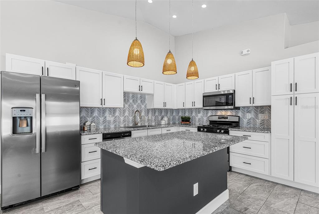 A modern kitchen features white cabinets, a dark gray island, granite countertops, and pendant lighting — 175 VILLAGE CIRCLE UNIT 32, LABELLE, FL