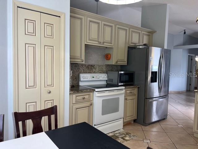 A kitchen features cream-colored cabinets, granite countertops, a white stove, and a stainless steel refrigerator — 4125 HAMPSHIRE VILLAGE COURT, ORLANDO, FL
