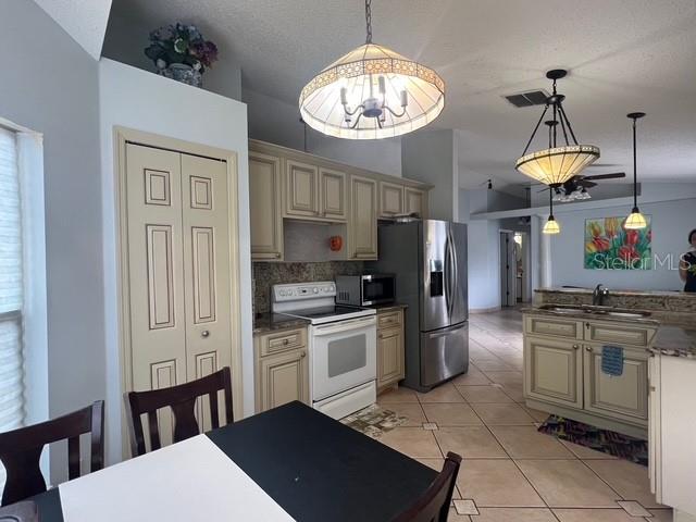 A kitchen features light-colored cabinetry, stainless steel appliances, tile flooring, and two hanging light fixtures — 4125 HAMPSHIRE VILLAGE COURT, ORLANDO, FL