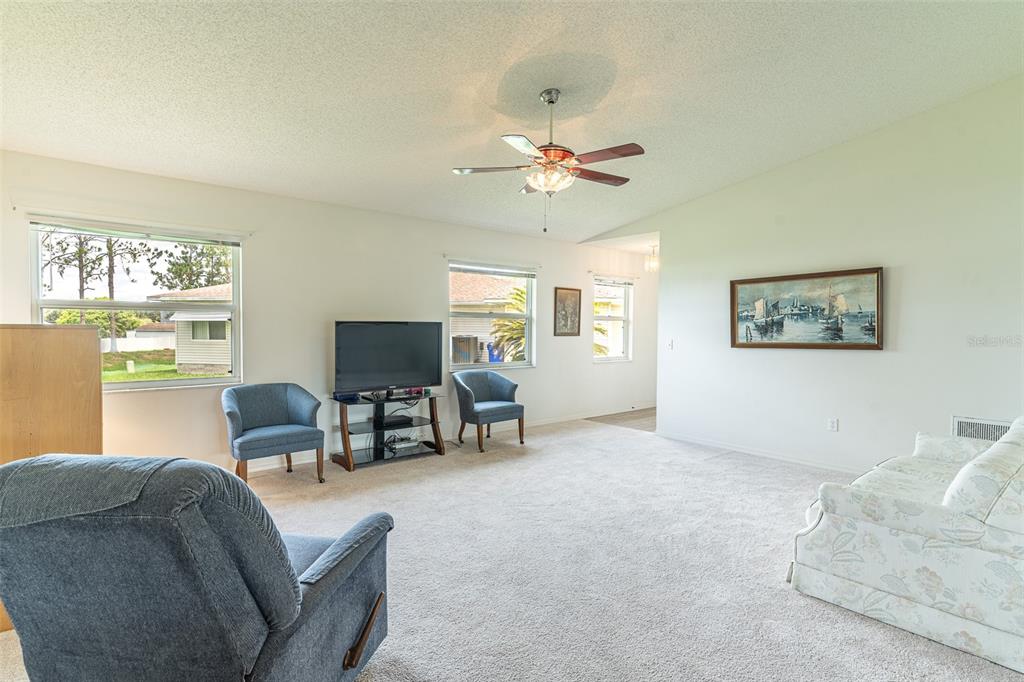A living room features beige carpeting, a ceiling fan, blue armchairs, and a floral sofa — 2260 GRAND CYPRESS DRIVE, LAKELAND, FL
