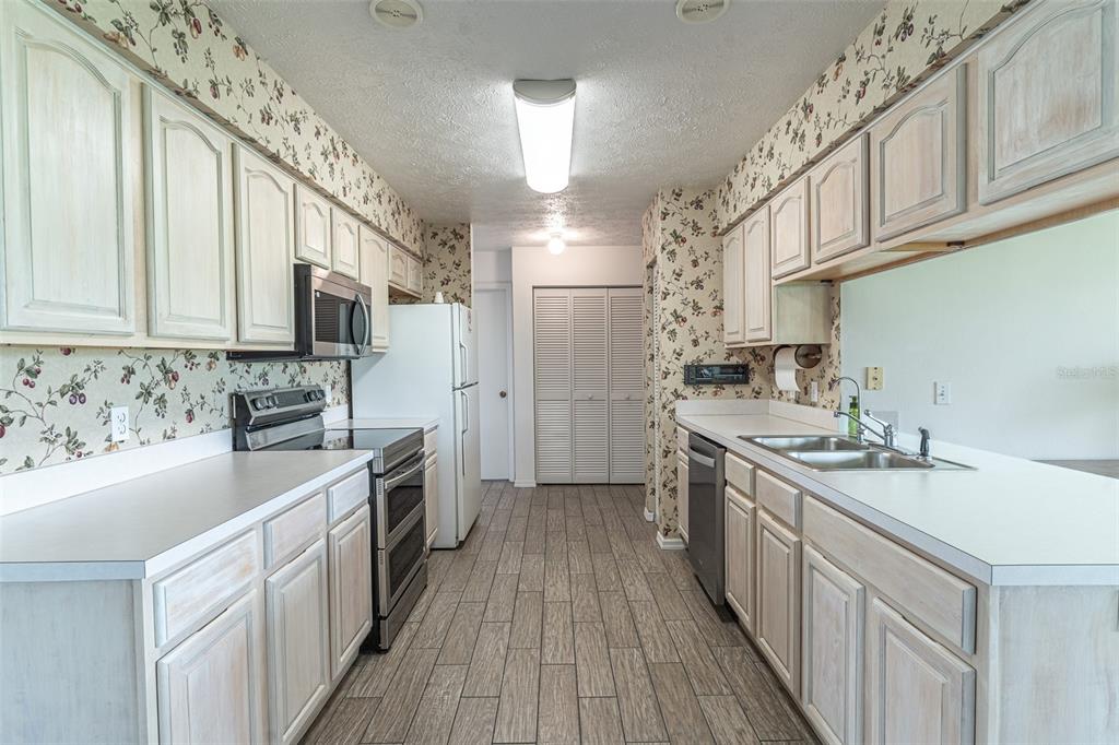 A galley kitchen features light wood cabinets, floral wallpaper, white countertops, and wood-look tile flooring — 2260 GRAND CYPRESS DRIVE, LAKELAND, FL