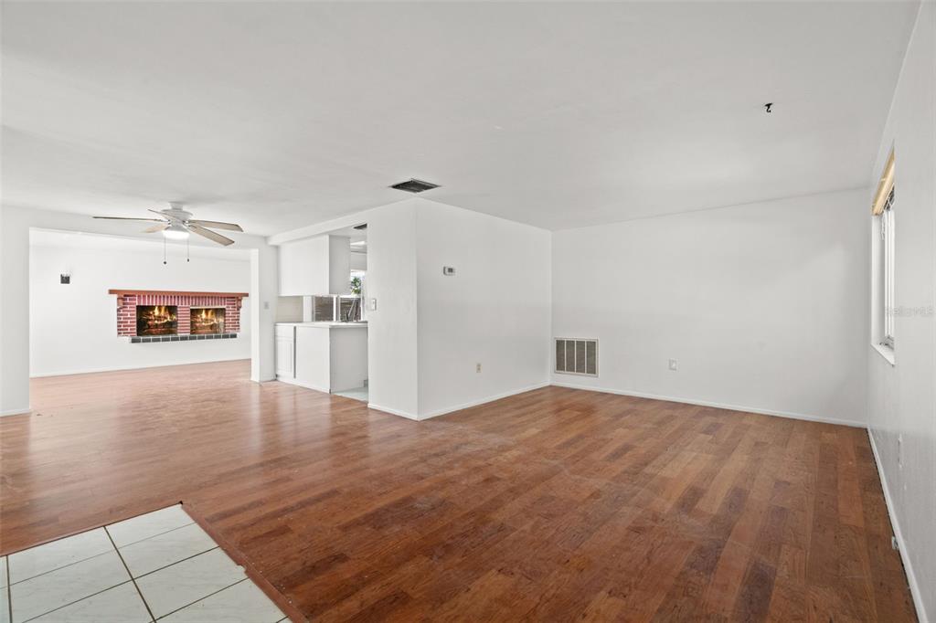 An open living area features wood flooring, white walls, and a brick fireplace in the background — 4312 NEWBURY DRIVE, NEW PORT RICHEY, FL