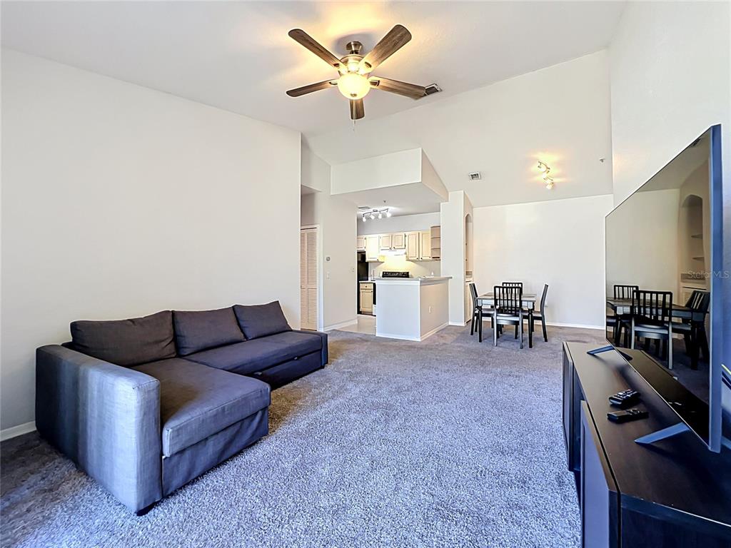 A living room with gray carpet, a sectional sofa, and an open kitchen area — 1150 LAKE SHADOW CIRCLE UNIT 3304, MAITLAND, FL