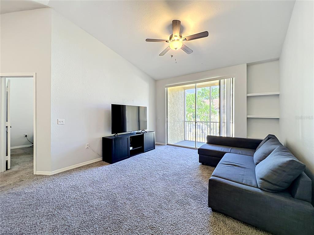 A living room features gray carpet, a dark sectional sofa, a television console, and a balcony — 1150 LAKE SHADOW CIRCLE UNIT 3304, MAITLAND, FL