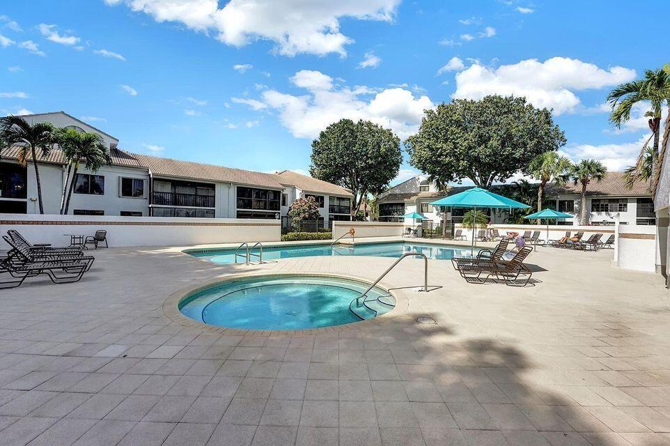 A swimming pool and hot tub are surrounded by a paved deck and apartment buildings — 7449 Glendevon Lane # 106, Delray Beach FL 33446, DELRAY BEACH, FL