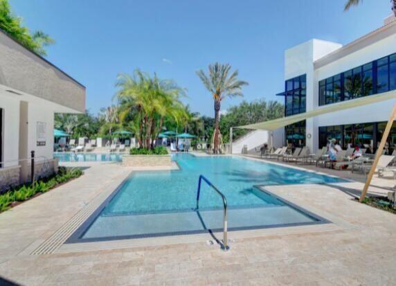 A swimming pool with a palm tree island sits between two modern buildings on a patio — 7449 Glendevon Lane # 106, Delray Beach FL 33446, DELRAY BEACH, FL