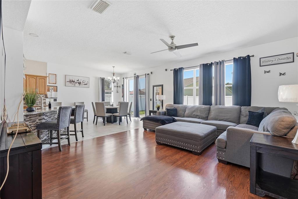 A living room with wood flooring, a large gray sectional, and an adjacent dining area — 5213 PRAIRIE VIEW WAY, WESLEY CHAPEL, FL