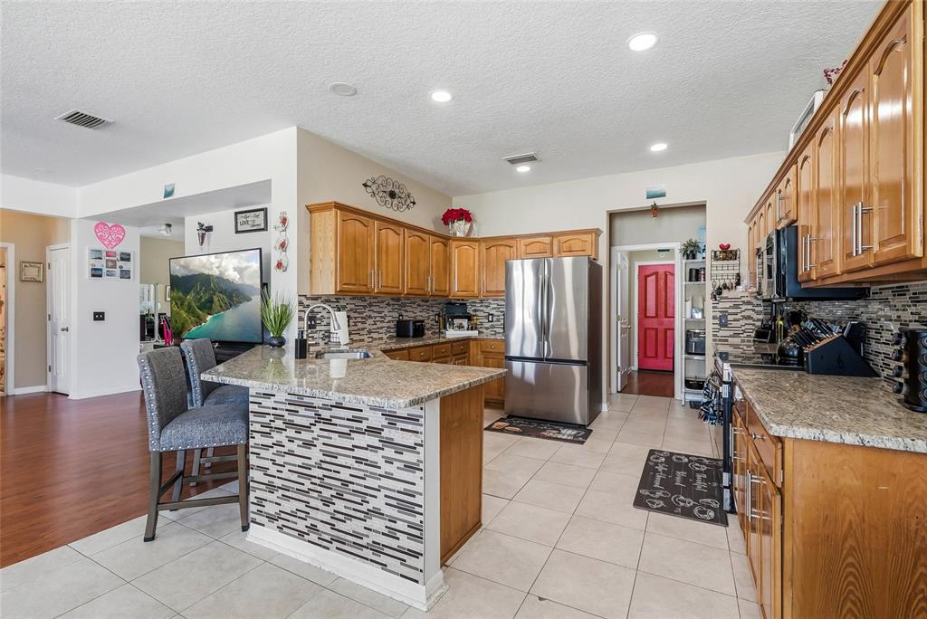 A kitchen features wood cabinets, granite countertops, a tiled island, and stainless steel appliances — 5213 PRAIRIE VIEW WAY, WESLEY CHAPEL, FL