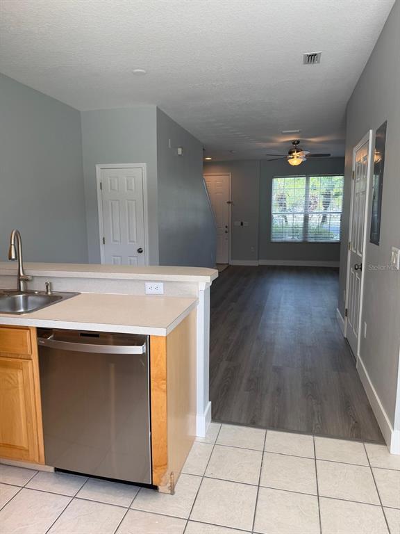 A kitchen with a stainless steel dishwasher and sink overlooks a living area with flooring — 11503 DECLARATION DRIVE, TAMPA, FL