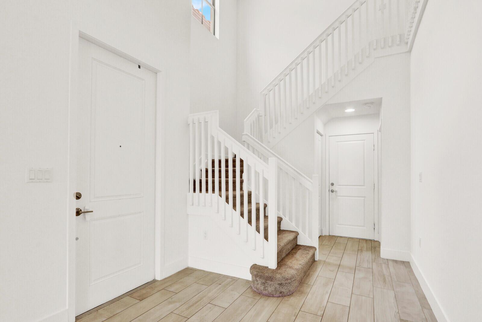 An entryway features white walls, wood-look tile flooring, a carpeted staircase, and two white doors — 4008 Sequoia Place, Riviera Beach FL 33410, RIVIERA BEACH, FL
