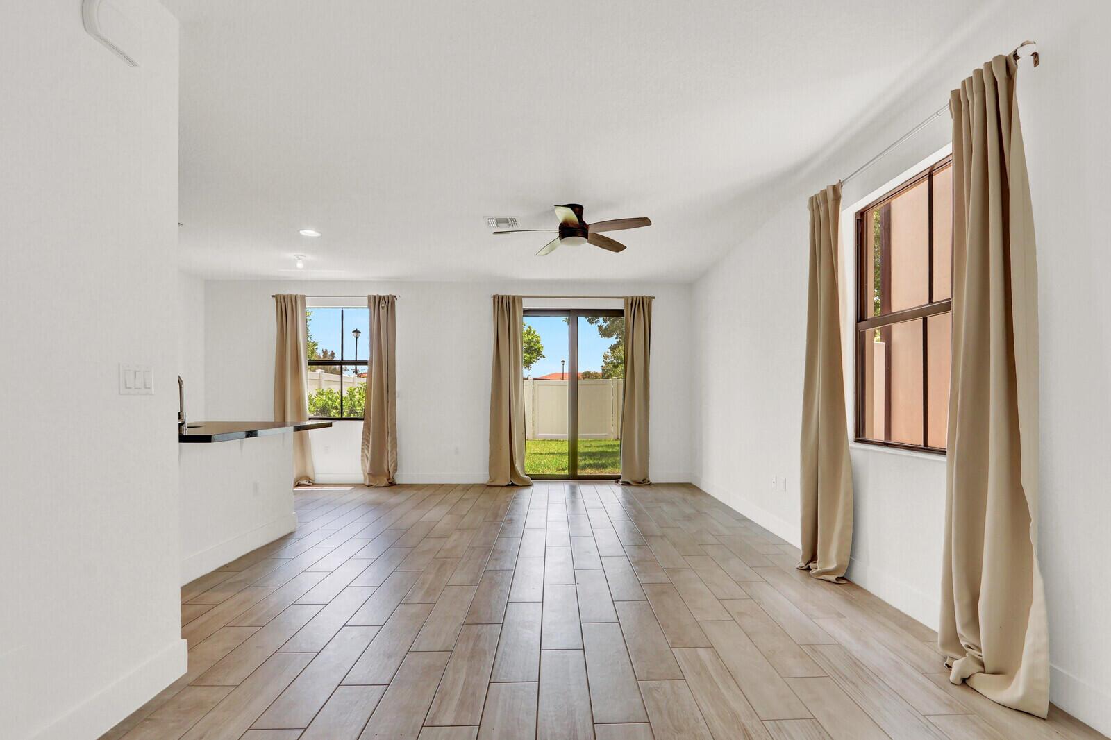 A bright, open-concept living area features light wood-look tile flooring, white walls, and sliding doors — 4008 Sequoia Place, Riviera Beach FL 33410, RIVIERA BEACH, FL