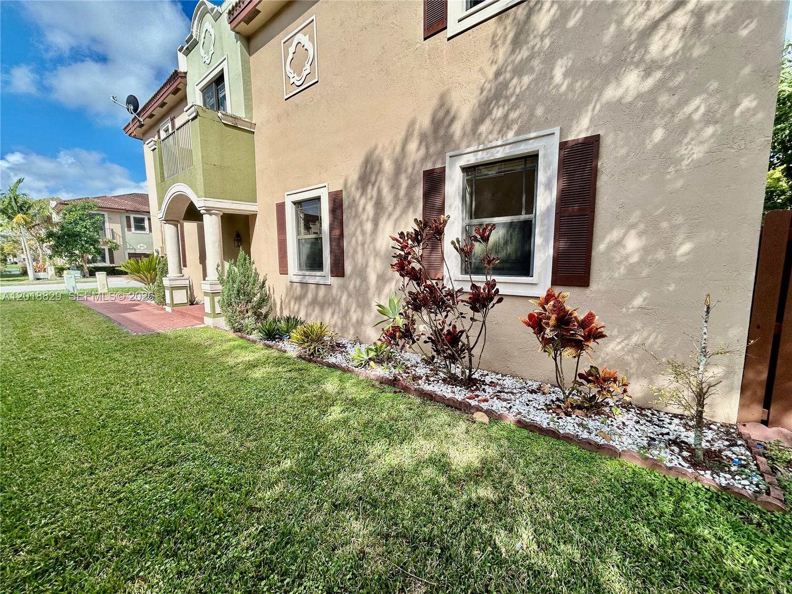 A beige two-story house exterior features brown shutters, a green balcony, and a landscaped garden — 607 NE 35th Ave # 607, Homestead FL 33033, HOMESTEAD, FL