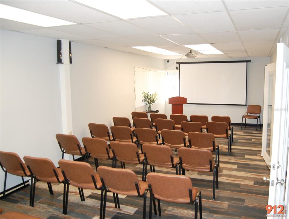 A meeting room features rows of brown chairs facing a projector screen and a podium — 912 DREW STREET STREET, CLEARWATER, FL