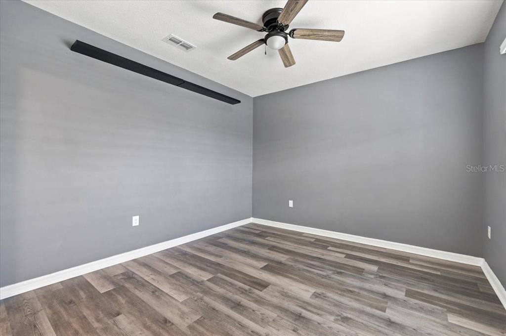 An empty room features gray walls, wood-look flooring, a ceiling fan, and a black accent beam — 2934 LONG POND DRIVE, LAKELAND, FL