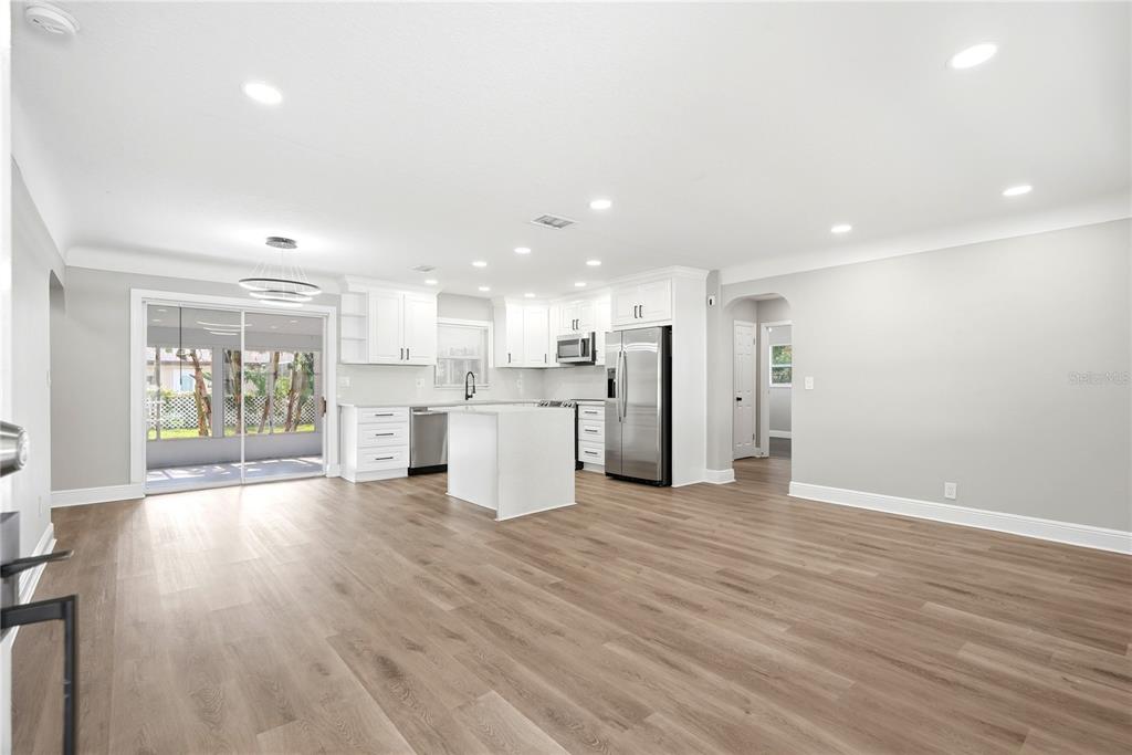 A bright, open-concept kitchen features white cabinetry, stainless steel appliances, and light wood-look flooring — 1628 S HIGHLAND AVENUE, CLEARWATER, FL