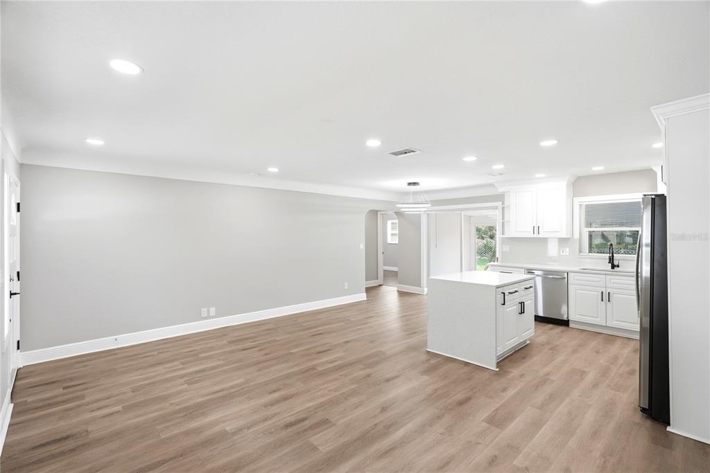 A bright, open-concept kitchen and living area features white cabinetry, a center island, and wood-look flooring — 1628 S HIGHLAND AVENUE, CLEARWATER, FL