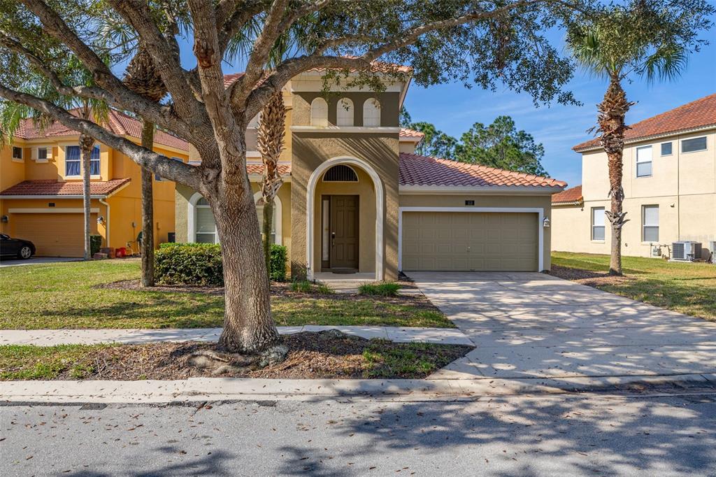 A two-story house with a tan stucco exterior, tile roof, and an attached two-car garage — 113 TIGER LILY COURT, DAVENPORT, FL