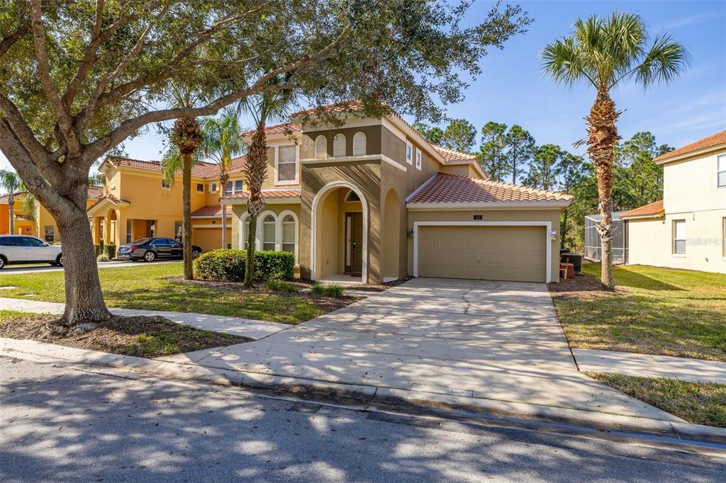 A two-story tan stucco house with a tile roof, arched entryway, and a two-car garage — 113 TIGER LILY COURT, DAVENPORT, FL