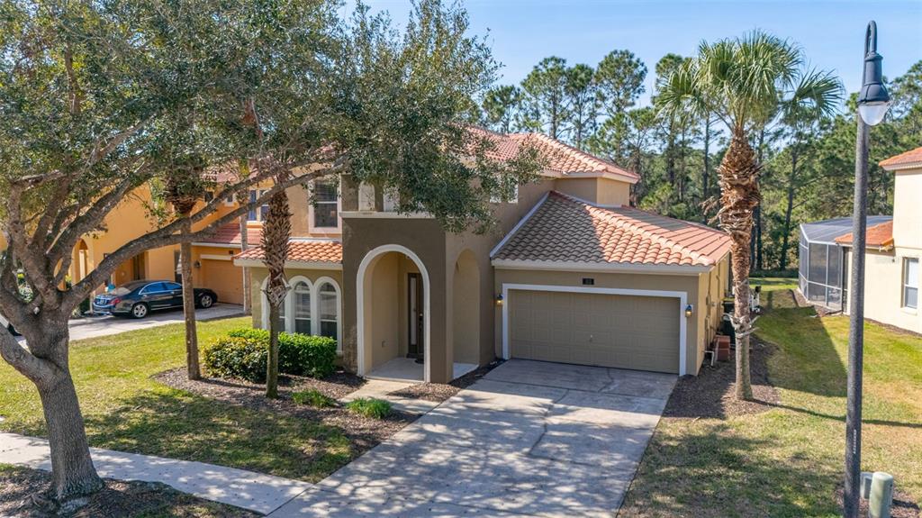A two-story tan stucco house with a tile roof, arched entryway, and attached garage — 113 TIGER LILY COURT, DAVENPORT, FL
