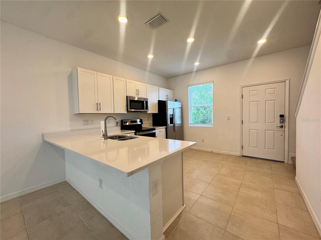 A kitchen features white cabinets, a quartz island, stainless steel appliances, and tile flooring — 8528 DAYBREAK STREET, SARASOTA, FL