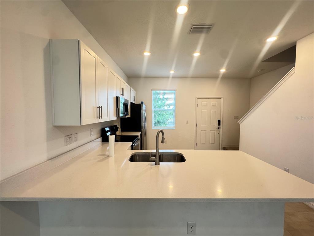 A kitchen features white cabinets, a quartz countertop island with a sink, and recessed lighting — 8528 DAYBREAK STREET, SARASOTA, FL