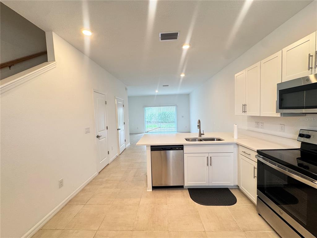 A kitchen with white cabinets, stainless steel appliances, and tile flooring overlooks an open living area — 8528 DAYBREAK STREET, SARASOTA, FL