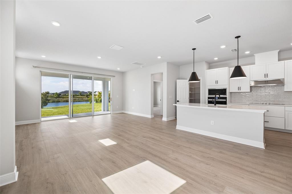 An open-concept kitchen and living area features light wood flooring, white cabinetry, and sliding glass doors — 11832 CATAWBA COVE, PARRISH, FL