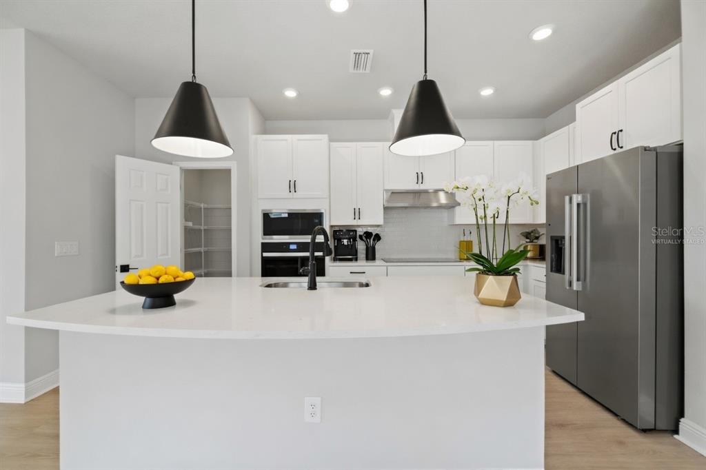 A modern kitchen features a large white island, stainless steel appliances, and white cabinetry — 11832 CATAWBA COVE, PARRISH, FL