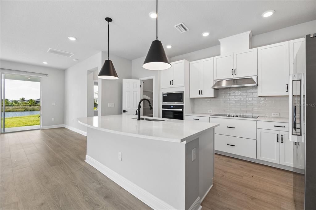 A modern kitchen features white cabinetry, a large quartz island, and a view of water — 11832 CATAWBA COVE, PARRISH, FL