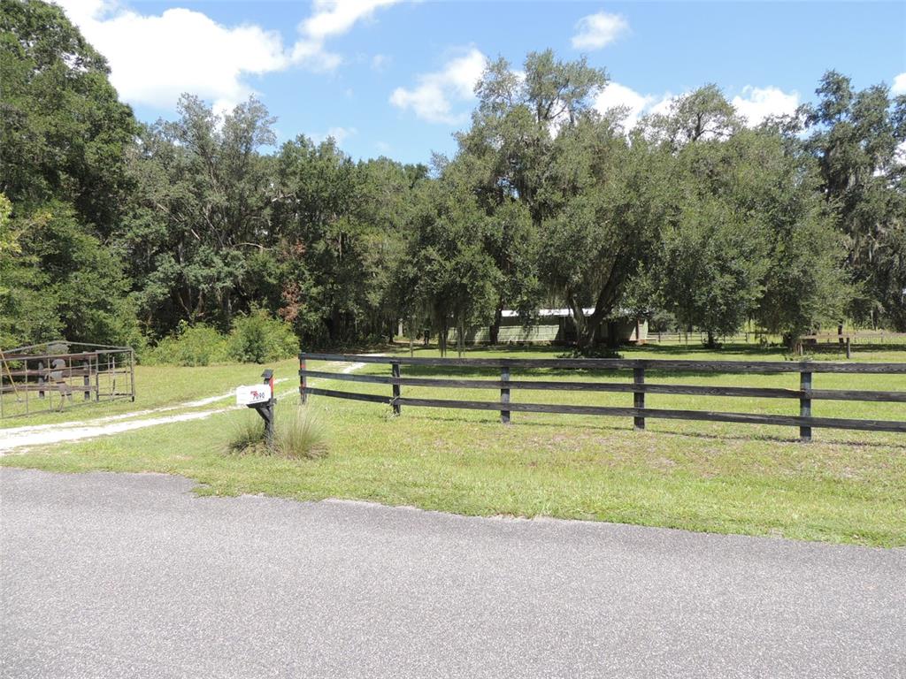 A gravel driveway leads through a wooden fence toward a house surrounded by large trees — 7090 SE 181ST COURT, MORRISTON, FL