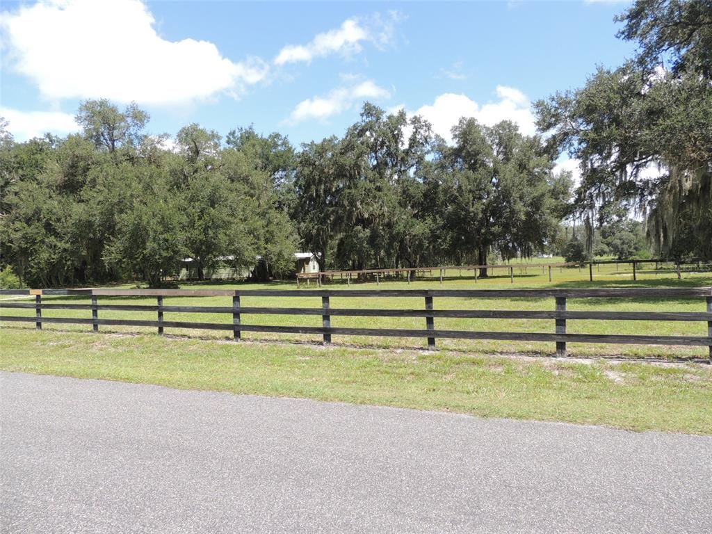 A wooden fence borders a grassy field with mature trees and a house in the background — 7090 SE 181ST COURT, MORRISTON, FL