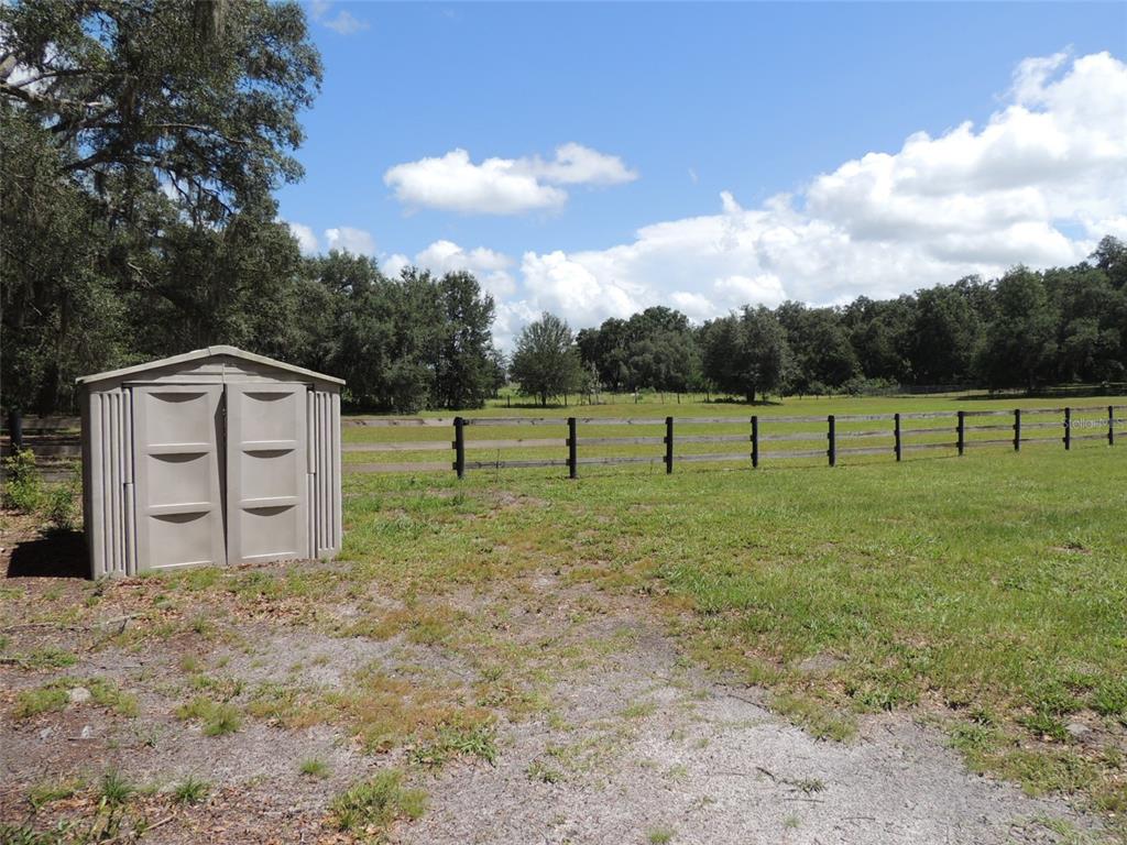 A small plastic storage shed sits on a grassy lot next to a wooden fence — 7090 SE 181ST COURT, MORRISTON, FL