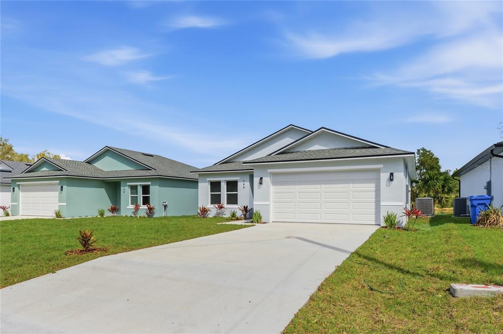 A light-colored single-story house with a two-car garage and a concrete driveway — 144 11TH AVENUE, OSTEEN, FL