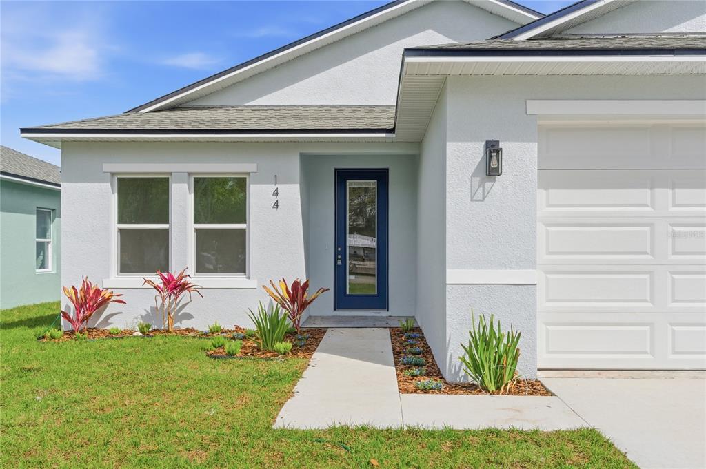 The exterior of a light-colored house features a blue front door and a concrete walkway — 144 11TH AVENUE, OSTEEN, FL