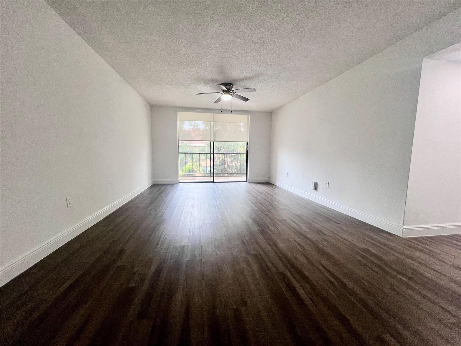 An empty room features dark wood-look flooring, white walls, and a sliding glass balcony door — 17350 NW 68th Avenue # 403, Hialeah FL 33015, HIALEAH, FL