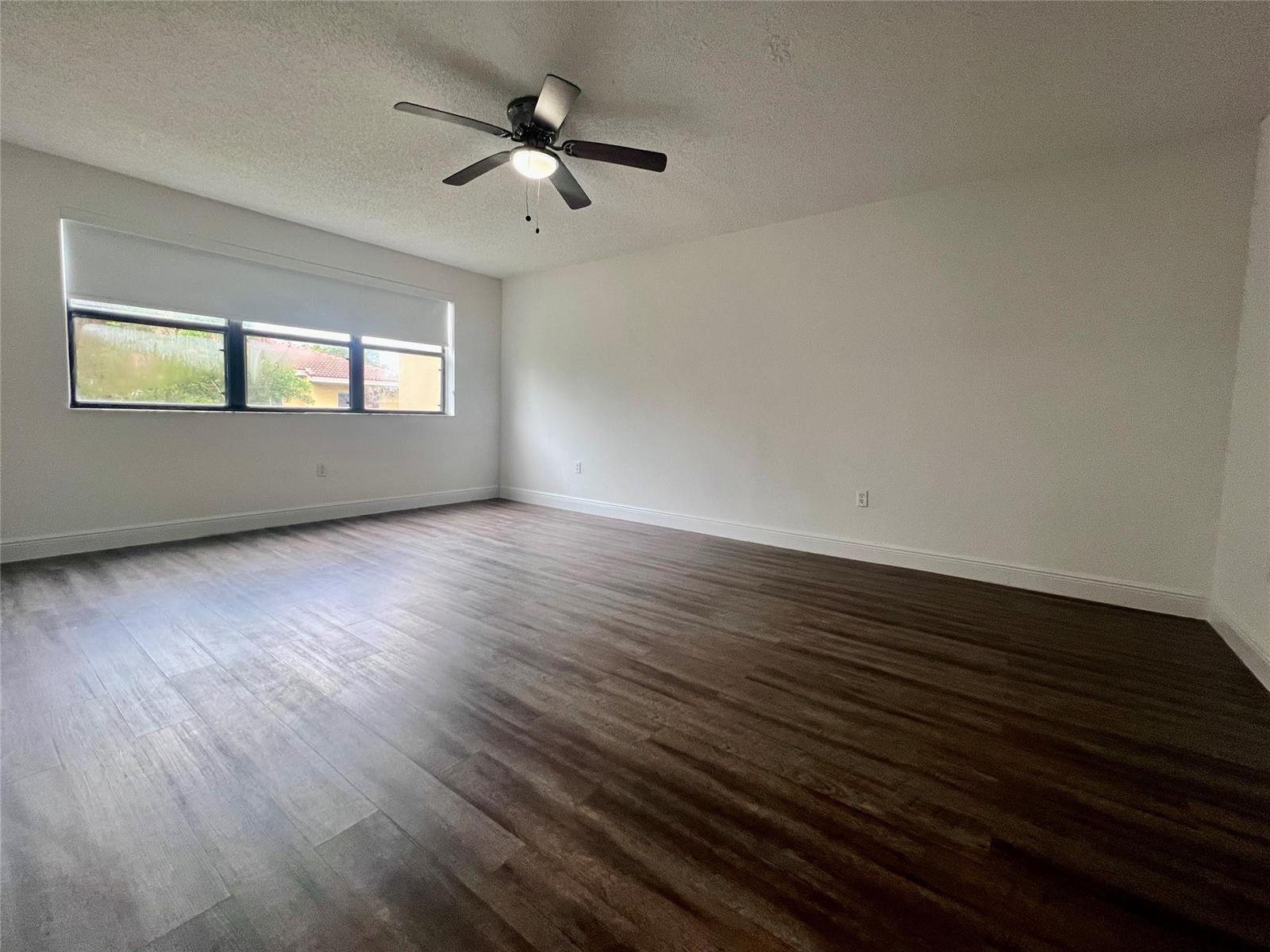 An empty room features dark wood-look flooring, white walls, a ceiling fan, and a window — 17350 NW 68th Avenue # 403, Hialeah FL 33015, HIALEAH, FL