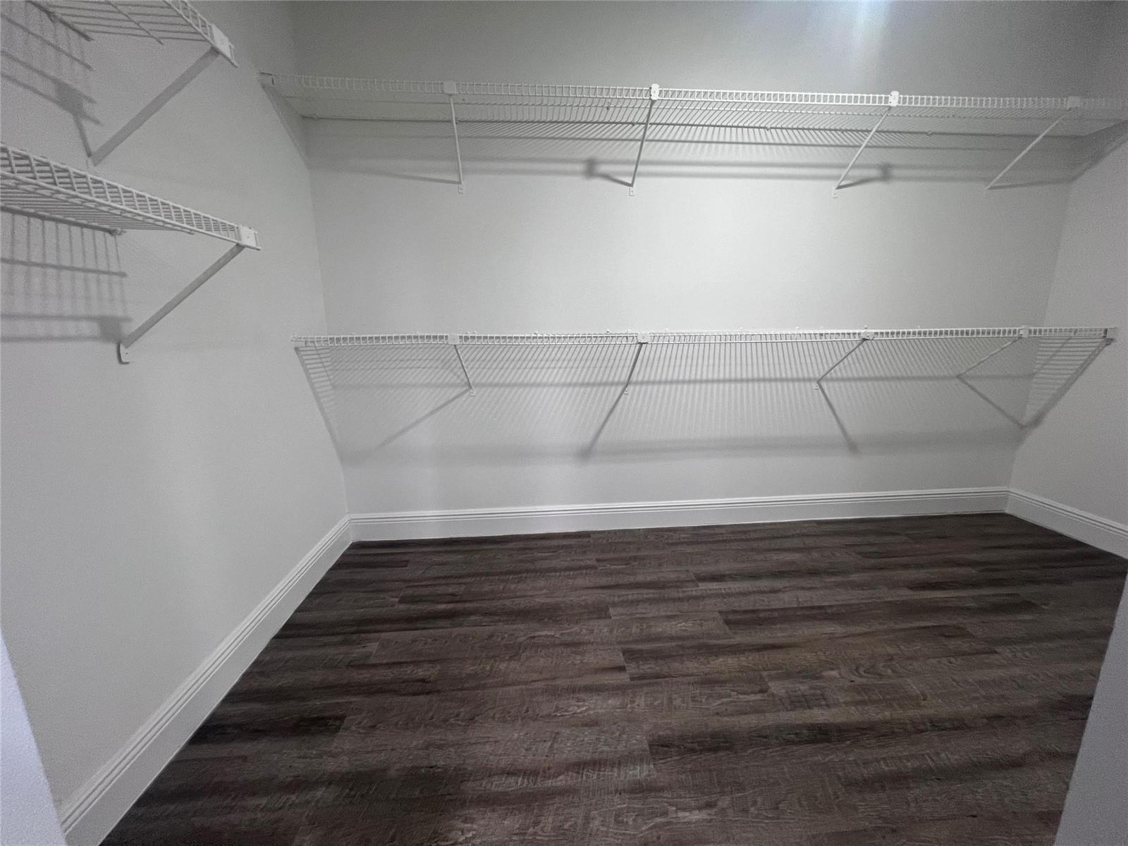 A walk-in closet features white wire shelving on the walls and dark wood-look flooring — 17350 NW 68th Avenue # 403, Hialeah FL 33015, HIALEAH, FL
