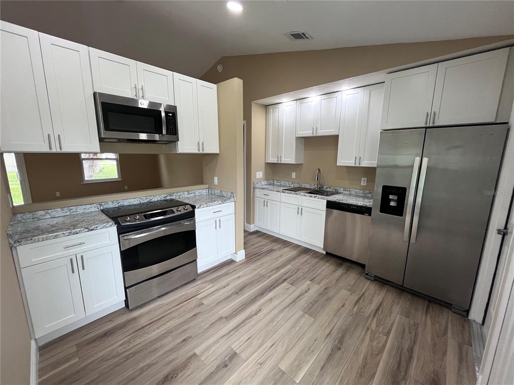 A kitchen features white cabinets, stainless steel appliances, and wood-look flooring — 3804 CAMBAY STREET, DELTONA, FL