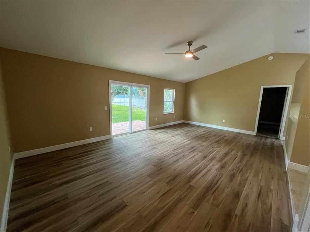 A spacious living room features vaulted ceilings, wood-look flooring, and sliding glass doors to a patio — 3804 CAMBAY STREET, DELTONA, FL