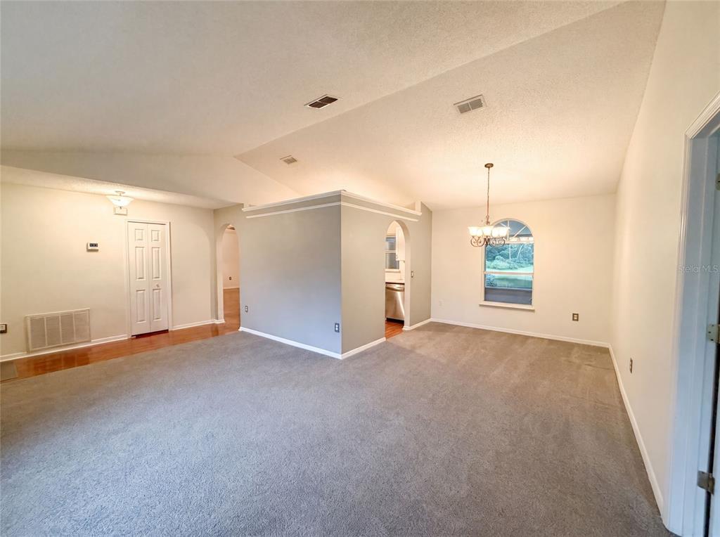 A living room with gray carpet, a vaulted ceiling, and an arched entryway to the kitchen — 29 VALENCIA CIRCLE, DEBARY, FL
